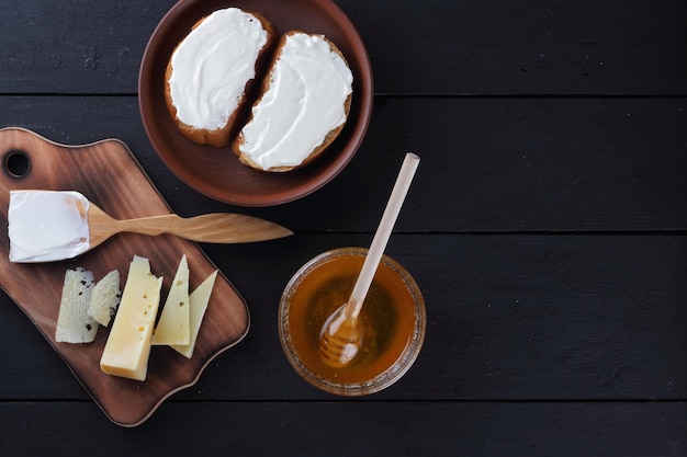 Cheese and sandwiches with soft cheese on a black wooden boards Hard cheese and cream with wooden cutlery Dairy products and honey on a dark background Top view