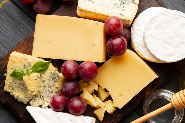 Cheese served with grapes and honey on grey textured surface