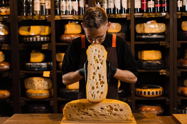 Cheese sommelier in food shop worker looking at limited maasdam\
natural aged and check quality handsome bearded man working in food\
store