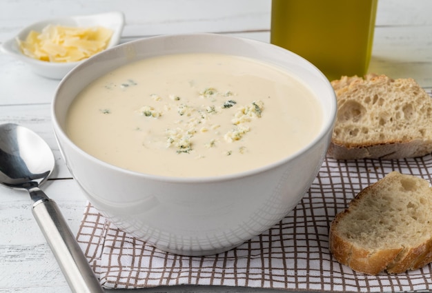 Cheese soup in a bowl with bread slices and seasonings over wooden table