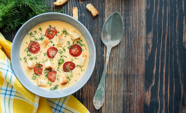 Cheese soup with grilled sausages and herbs on a wooden table. Copy space.