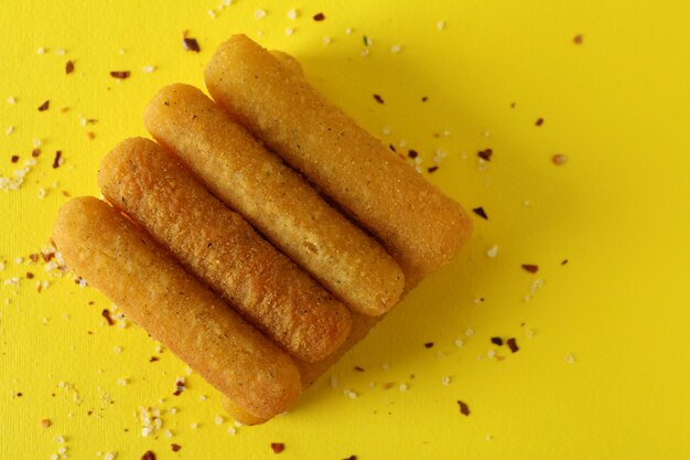 Cheese sticks and spices on yellow background