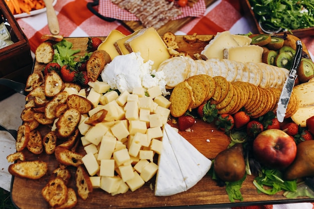 Сыр, овощи, нарезанное мясо и салат, подаваемый на красной скатерти в парке