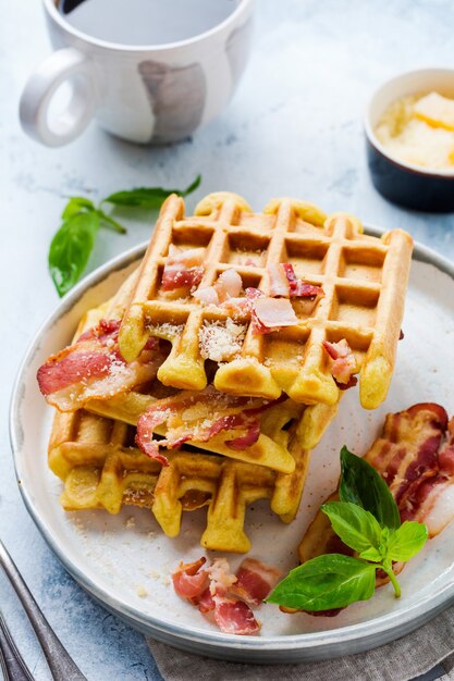 Cheese Waffles with fried bacon, egg and parmesan cheese with spices and basil for breakfast on light old concrete surface