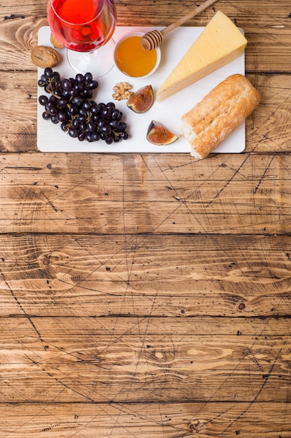 Cheese, wine, baguette grapes figs honey and snacks on the rustic wooden table top with copy space.