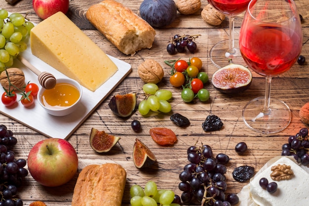 Cheese, wine, baguette grapes figs honey and snacks on the rustic wooden table top.