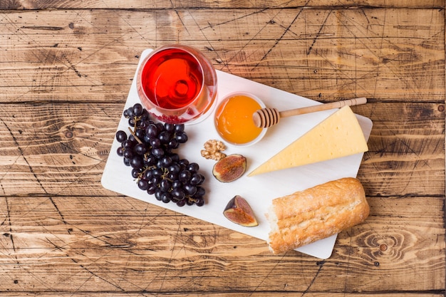 Cheese, wine, baguette grapes figs honey and snacks on the rustic wooden table top.