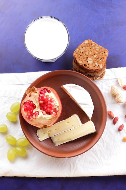 Сыр с фруктами, орехами, темным хлебом и стаканом молока на белой салфетке на синем фоне. Отличный продукт для завтрака.