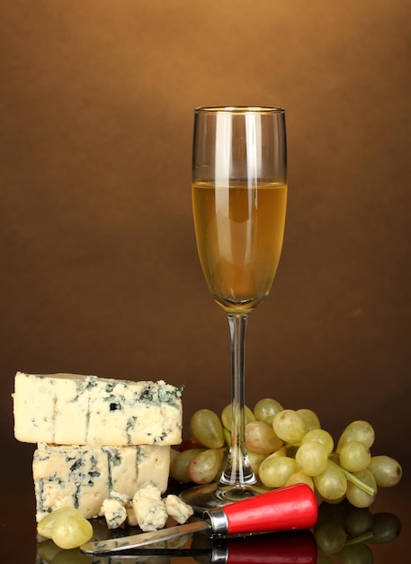 Photo cheese with mold and goblet of wine on brown background closeup