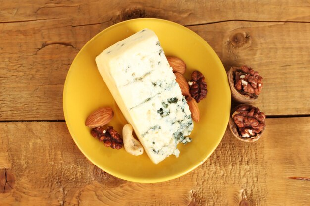 Cheese with mold and walnuts on the plate on wooden background closeup