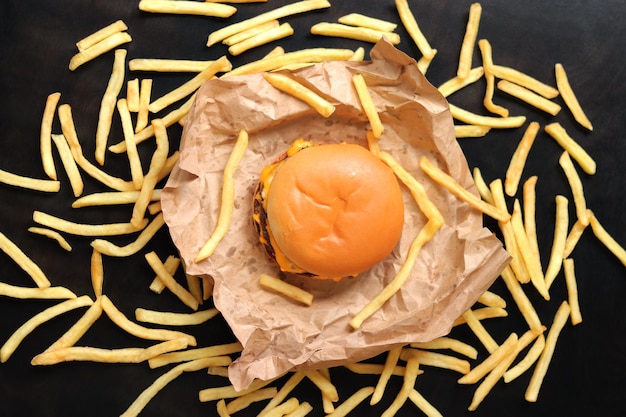 Photo cheeseburger on craft paper french fries on a dark wooden table top view menu background