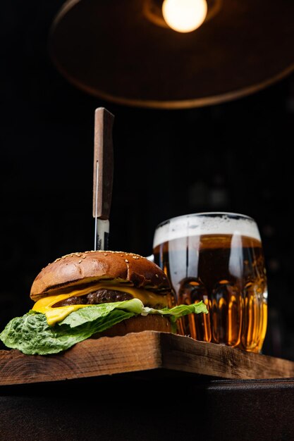 A cheeseburger and a glass of beer sit on a table.