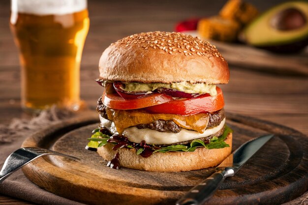 Cheeseburger made from rye bun with tomato slice and melted\
cheese on a roasted beef and lettuce leaf on a wooden table with a\
glass of beer