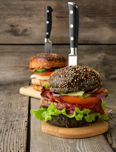 Foto cheeseburger met zwart broodje, vlees en groenten op een houten tafel, fast food en mes