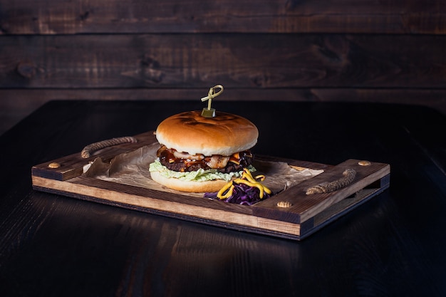 Cheeseburger on a wooden tray in a restaurant, on a dark background.