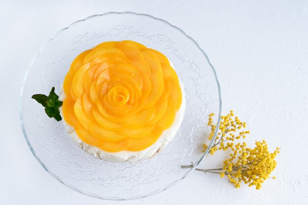 Cheesecake decorated with peaches and yellow flowers on a white background. Copy space.