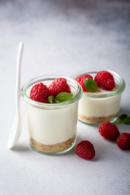 Cheesecake in a glass decorated with raspberries and mint on a gray table