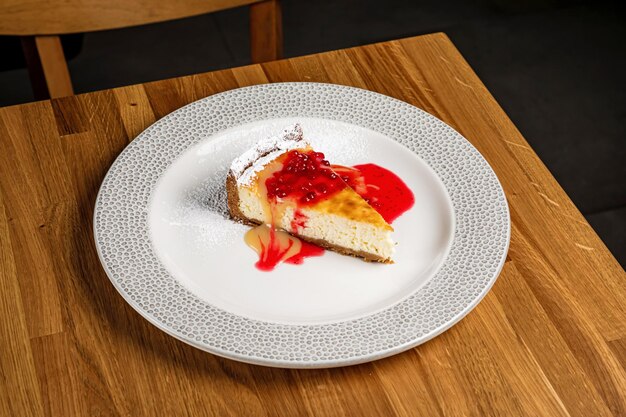 Cheesecake met bessensaus geserveerd op een witte plaat op een houten tafel in een restaurant