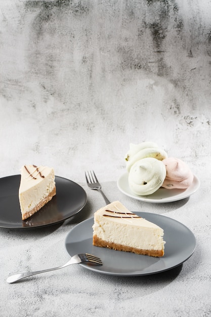 Cheesecake New York or classic cheesecake with cup of coffee on white table. Closeup view. Tasty breakfast. Piece of cake on black plate, white cup on white marble background. Vertical photo.