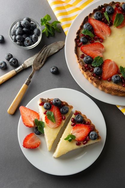 Cheesecake slice, with fresh berries and mint for dessert. Gray background.