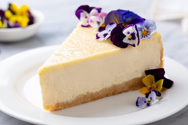 Cheesecake versierd met eetbare bloemen op witte plaat Marmeren achtergrond Close up