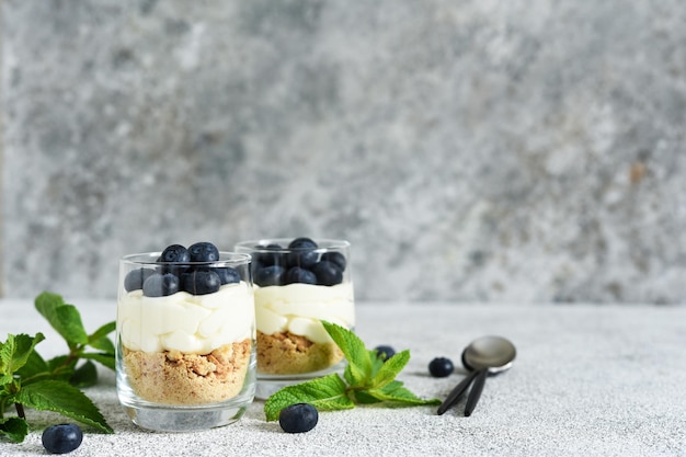 Cheesecake with cookies and berries in a glass on a light concrete background.