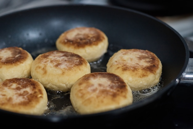 Cheesecakes are fried in a frying pan the cook turns the dough with a spoon close up the background is blurred