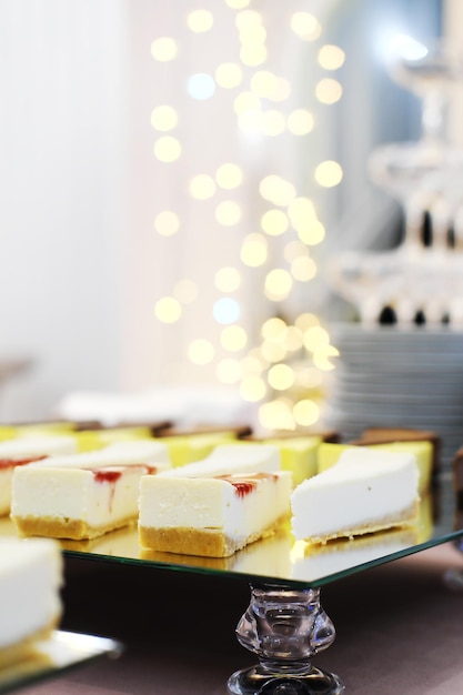 Cheesecakes on a mirror tray stand on a buffet table against the background of golden bokeh