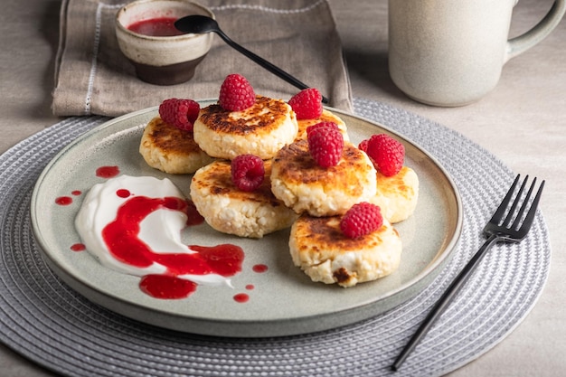 Cheesecakes of syrniki op een rond bord met frambozen, zure room en frambozensiroop.
