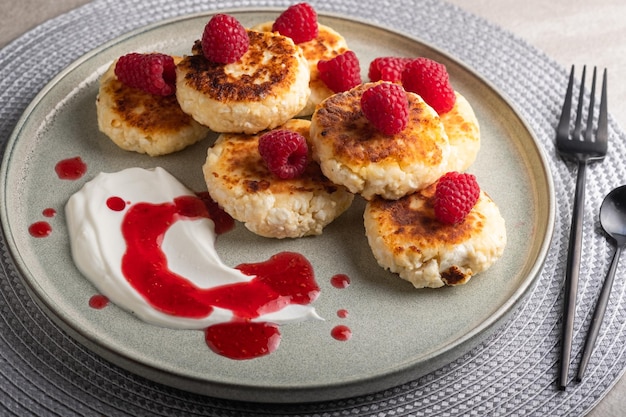 Cheesecakes or syrniki on a round plate with raspberry, sour cream and raspberry syrup.