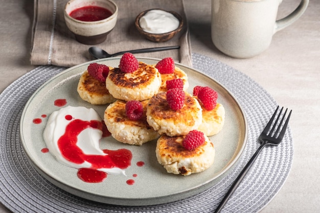 Cheesecakes or syrniki on a round plate with raspberry, sour cream and raspberry syrup.