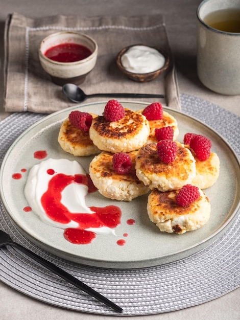 Cheesecakes or syrniki on a round plate with raspberry, sour cream and raspberry syrup.