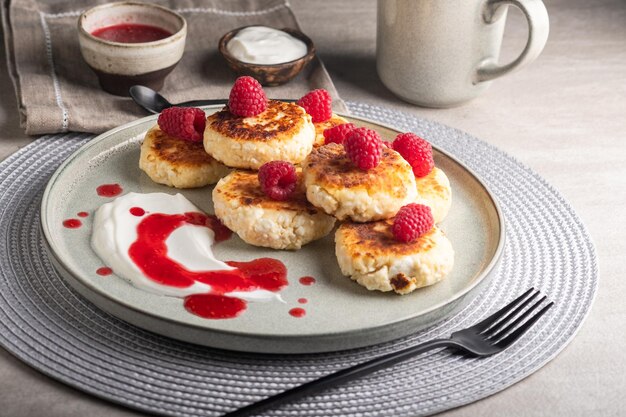 Cheesecakes or syrniki on a round plate with raspberry, sour cream and raspberry syrup.