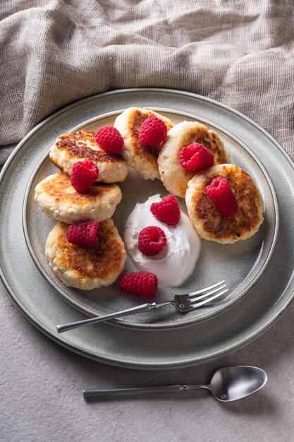 Cheesecakes or syrniki on a round plate with raspberry, sour cream and raspberry syrup.