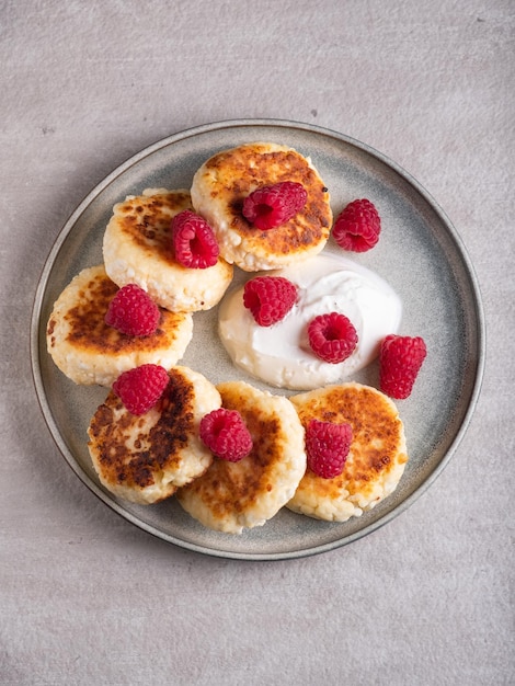 Cheesecakes or syrniki on a round plate with raspberry, sour cream and raspberry syrup.