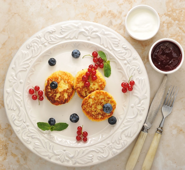 Cheesecakes with cottage cheese on a plate with sour cream and jam