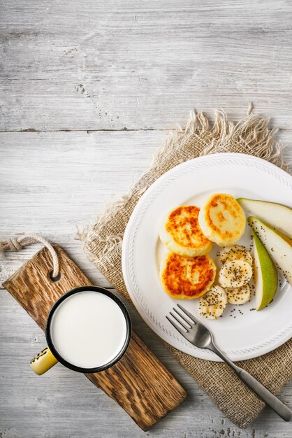 Cheesecakes with pear and milk on a white wooden table