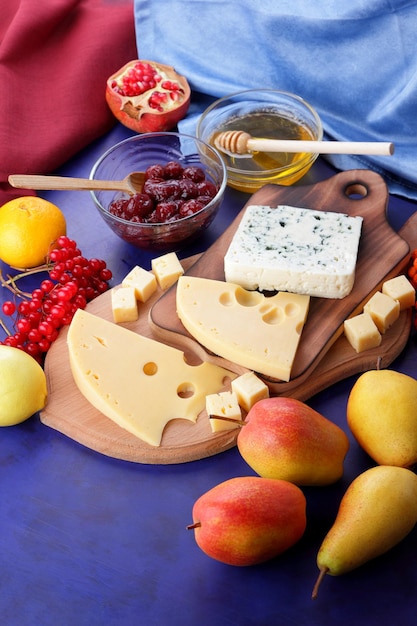 Formaggi con miele e limone su sfondo blu con tovaglioli blu e rossi due tipi di formaggio su una tavola di legno con frutti e bacche in primo piano