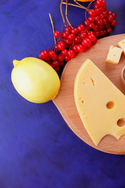 Cheeses with honey and lemon on a blue background with blue and red napkins Two types of cheese on a wooden board with fruits and berries closeup