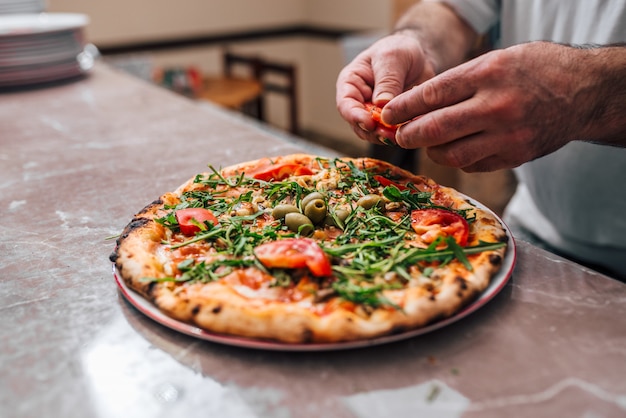 Cuoco unico che aggiunge pomodori come tocco finale sulla pizza.