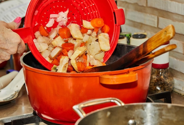 Chef adds boiled vegetables to chicken legs fried in pan