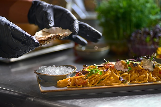 The chef adds to the pasta, fresh oyster on a plate.