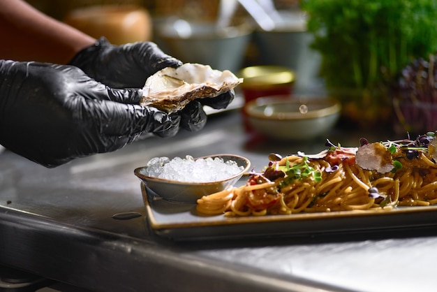 The chef adds to the pasta, fresh oyster on a plate.