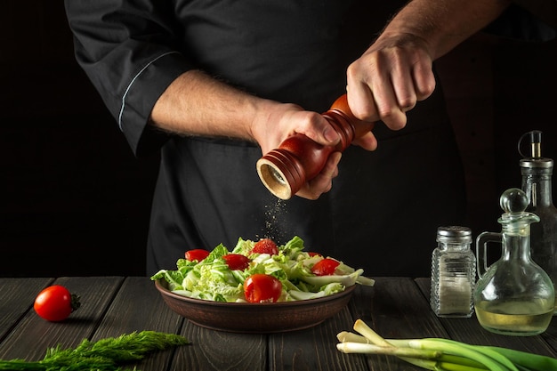 Chef adds peppers to a fresh vegetable salad in a restaurant kitchen