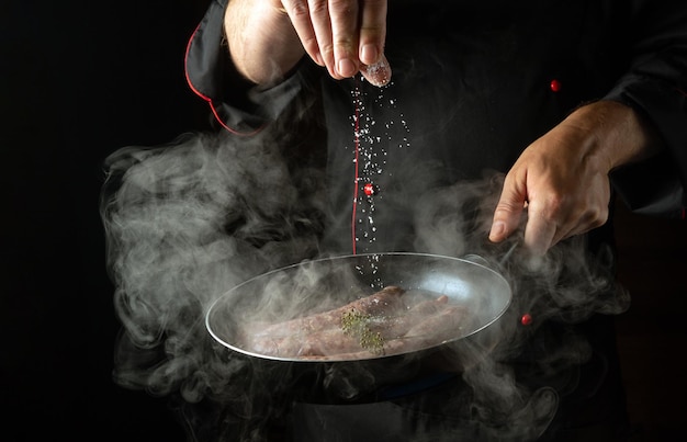 The chef adds salt to a hot frying pan with sausages Menu or recipe concept for hotel