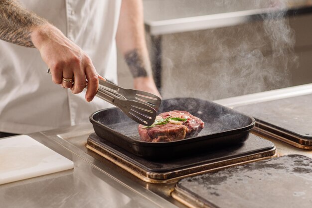 Chef bakt een biefstuk in de pan in de restaurantkeuken