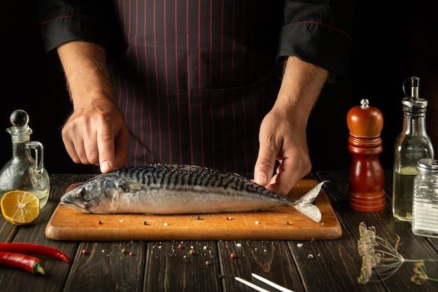 Chef bereidt makreel of Scomber in de keuken van het hotel Het concept van het koken van vis op een donkere achtergrond