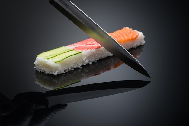 Chef bereidt sushi, snijdt met een mes. sushi op zwarte achtergrond met reflectie