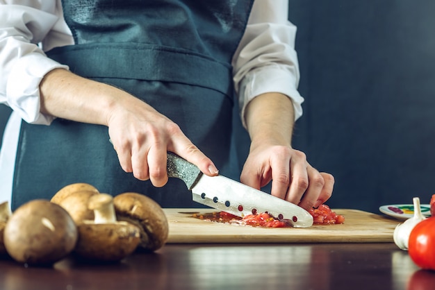 Chef in black apron cutting tomatoes with a knife