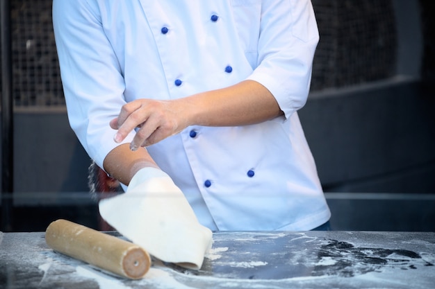 The chef in black apron makes pizza dough with your hands on the table. 